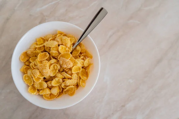 Top view of bowl with corn flakes and spoon on marble surface — Stock Photo