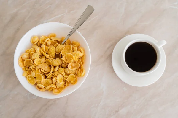 Верхний вид чаши с кукурузными хлопьями и ложкой возле чашки кофе на мраморной поверхности — стоковое фото
