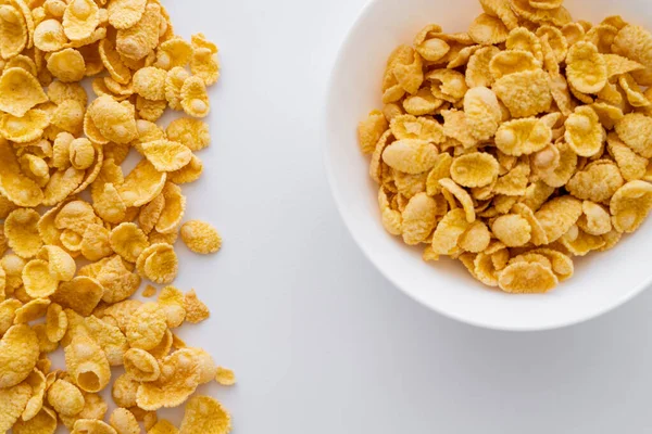 Top view of dry and crispy corn flakes near bowl isolated on white — Stock Photo