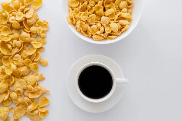 Vista superior da tigela com flocos de milho perto de xícara de café preto isolado em branco — Fotografia de Stock