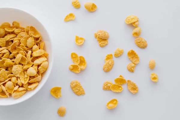 Top view of crispy and yellow corn flakes near bowl isolated on white — Stock Photo