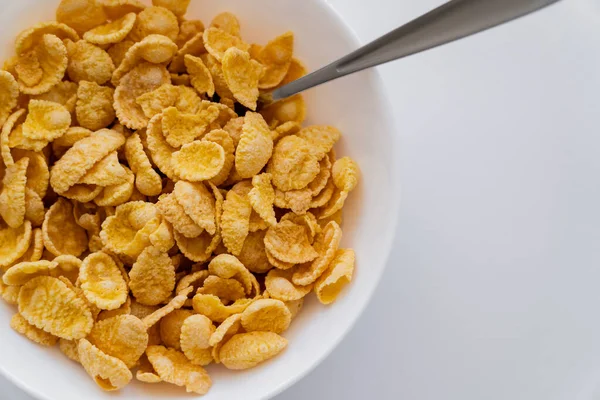 Top view of crispy and yellow corn flakes in bowl with spoon isolated on white — Stock Photo