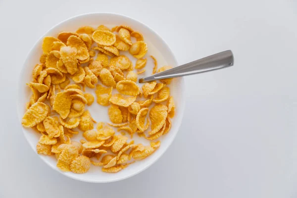 Blick von oben auf knusprige Cornflakes in Schüssel mit Löffel und Milch isoliert auf weiß — Stockfoto