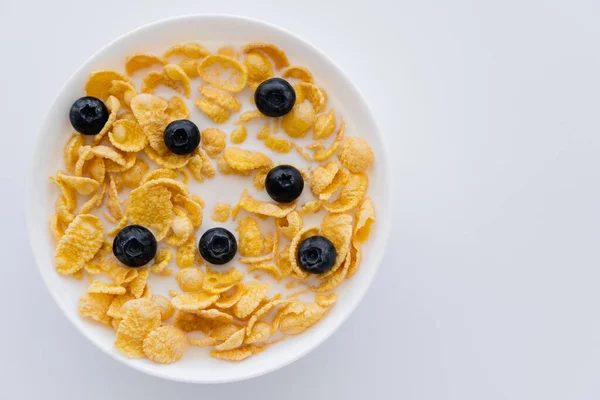 Vue du dessus des flocons de maïs croustillants dans un bol avec du lait biologique et des bleuets isolés sur du blanc — Photo de stock