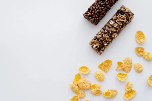 Vista superior de copos de maíz crujientes cerca de sabrosas barras de granola aisladas en blanco - foto de stock