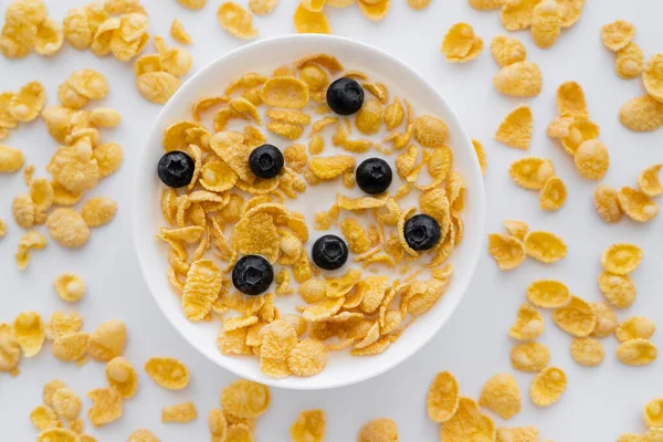 Vista dall'alto di gustosi corn flakes in ciotola con latte biologico e mirtilli freschi isolati su bianco — Foto stock