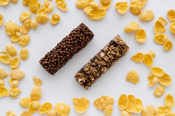 Top view of tasty granola bars around crunchy corn flakes isolated on white — Stock Photo