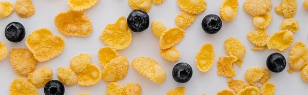 Top view of crispy corn flakes near tasty blueberries on white background, banner — Stock Photo