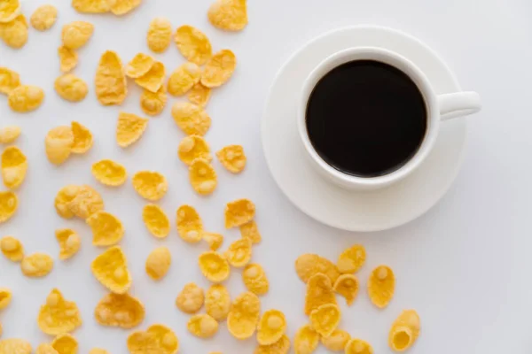 Vista superior de copos de maíz cerca de taza de café negro y platillo aislado en blanco - foto de stock