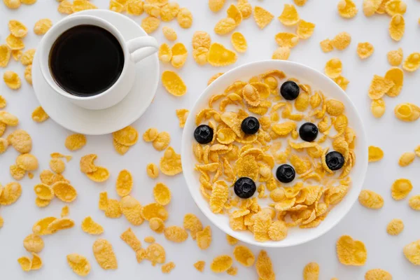 Vue du dessus du bol avec des flocons de maïs et du lait près de tasse de café noir isolé sur blanc — Photo de stock