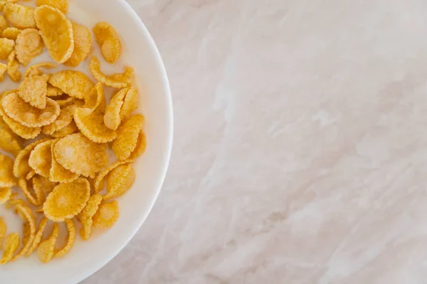 Top view of crispy corn flakes in bowl with spoon and milk on marble surface — Stock Photo