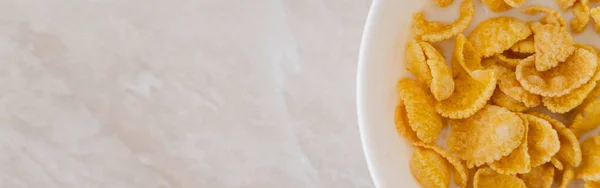 Top view of crispy corn flakes in bowl with spoon and milk on marble surface, banner — Stock Photo