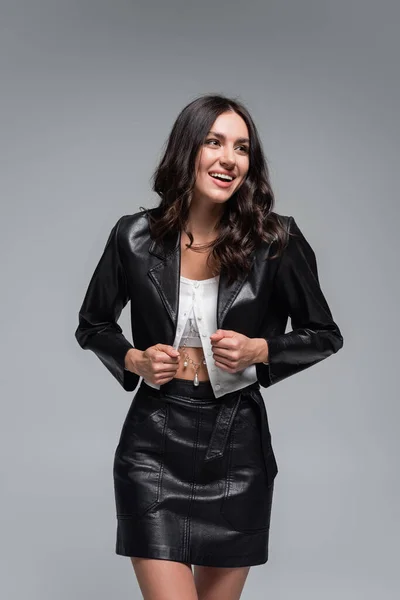 Happy young woman in stylish black leather jacket and skirt isolated on grey — Stock Photo