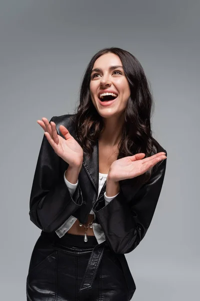 Excited young woman in stylish black leather jacket gesturing isolated on grey — Stock Photo