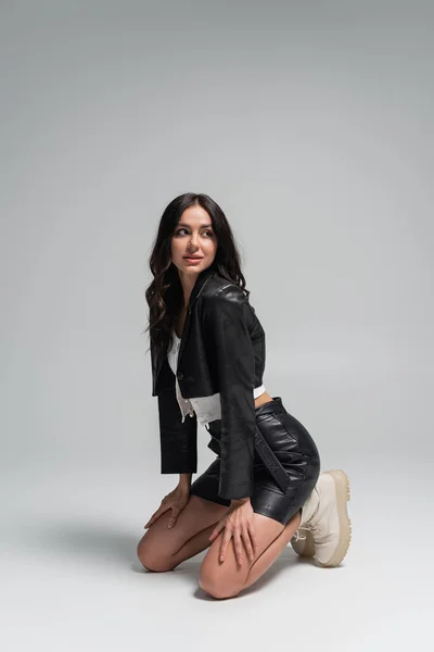 Full length of young woman in stylish autumnal outfit and beige boots sitting on grey — Stock Photo