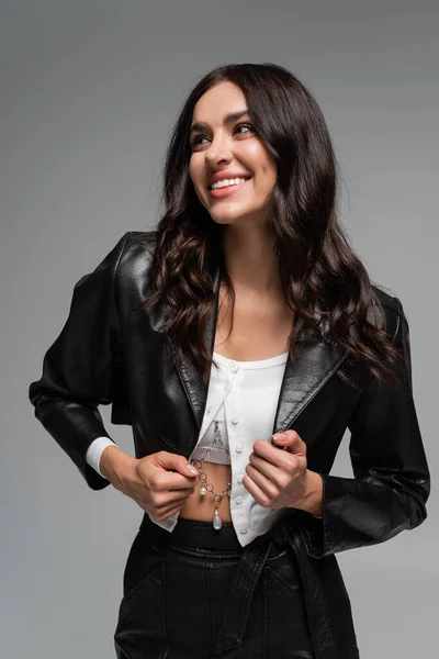 Happy young woman adjusting black leather jacket isolated on grey — Stock Photo