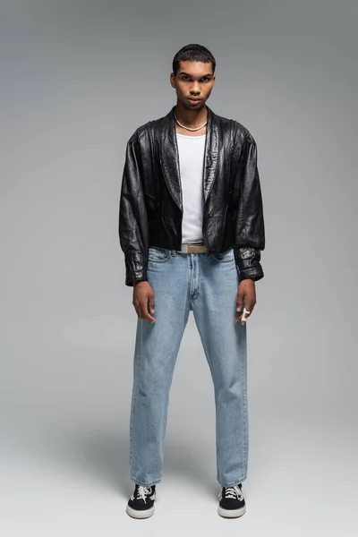 Full length of young african american man in jeans and leather jacket on grey — Stock Photo