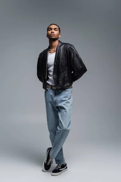 Full length of stylish african american man in autumnal outfit posing with crossed legs on grey — Stock Photo