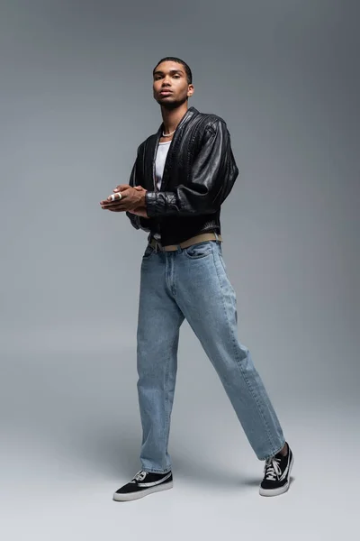 Full length of african american man in stylish autumnal outfit posing on grey — Stock Photo