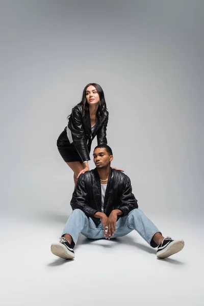 Full length of stylish woman in leather jacket posing with young african american man on grey — Stock Photo