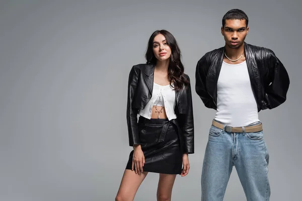 Stylish woman in leather outfit posing with young african american man isolated on grey — Stock Photo