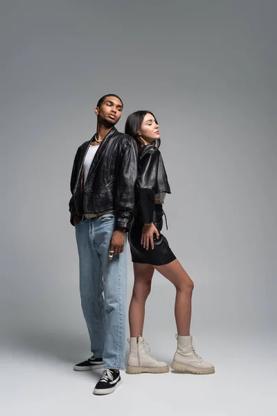 Full length of stylish interracial couple standing in trendy autumnal outfits on grey — Stock Photo