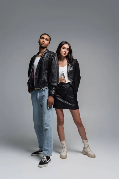 Piena lunghezza di giovane coppia interrazziale in abiti autunnali alla moda in piedi sul grigio — Foto stock