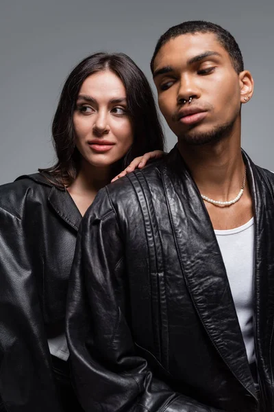 Young woman and stylish african american man in leather jackets isolated on grey — Stock Photo