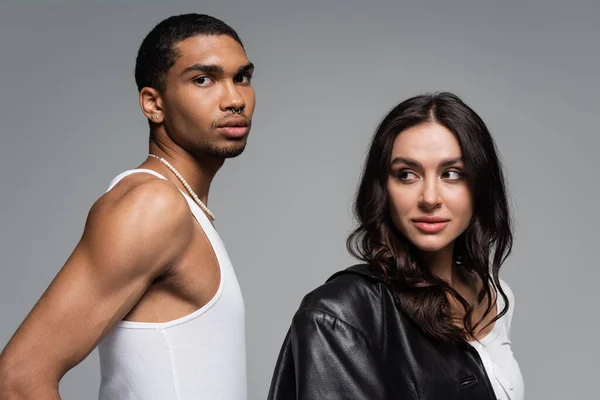 Young woman in leather jacket looking at african american man in tank top isolated on grey — Stock Photo