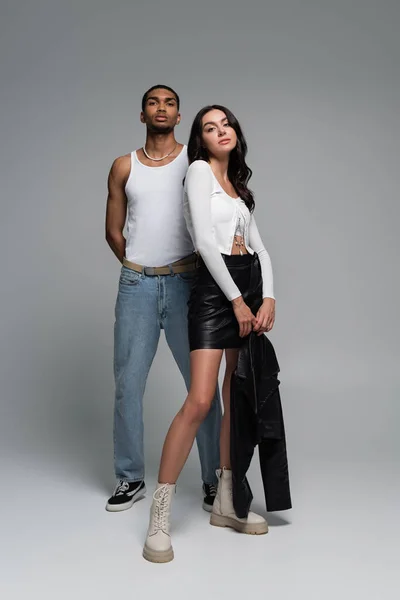 Pleine longueur de jeune homme afro-américain en débardeur et jolie femme en tenue élégante posant sur gris — Photo de stock