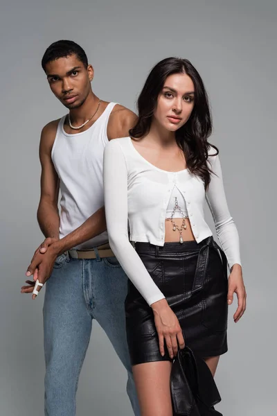 Young african american man in tank top and pretty woman in leather skirt posing isolated on grey — Stock Photo