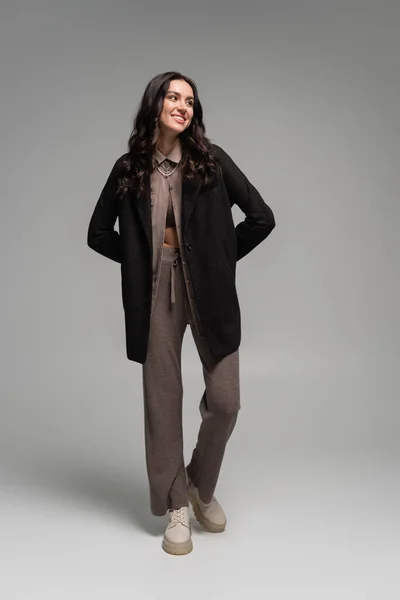 Full length of happy young woman in black blazer and knitted trousers posing on grey — Stock Photo