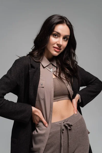 Brunette jeune femme en blazer noir posant avec les mains sur les hanches isolé sur gris — Stock Photo