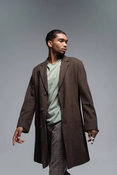 Young african american man in woolen coat standing isolated on grey — Stock Photo