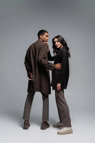 Full length of stylish interracial models in autumnal trendy clothes posing on grey — Stock Photo