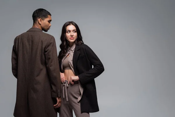 Young african american man in woolen coat near stylish woman in black blazer isolated on grey — Stock Photo