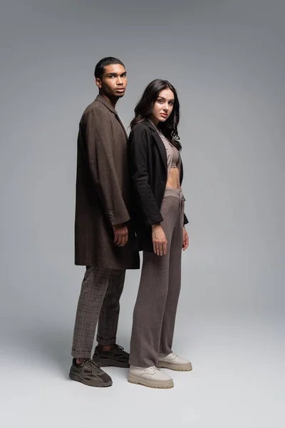 Full length of stylish interracial couple in autumnal outfits standing together on grey — Stock Photo