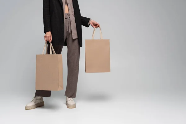 Vue recadrée de la jeune femme en tenue automnale élégante debout avec des sacs à provisions sur gris — Photo de stock