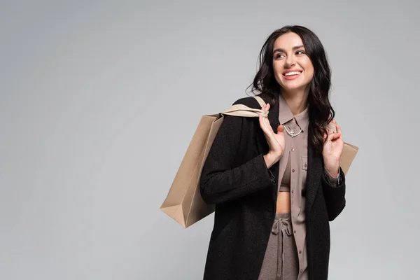 Cheerful young woman in black blazer holding shopping bags isolated on grey — Stock Photo