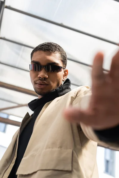Low angle view of young african american in stylish sunglasses standing with outstretched hand under roof — Stock Photo