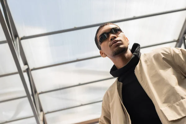 Low angle view of african american in stylish sunglasses standing under roof — Stock Photo