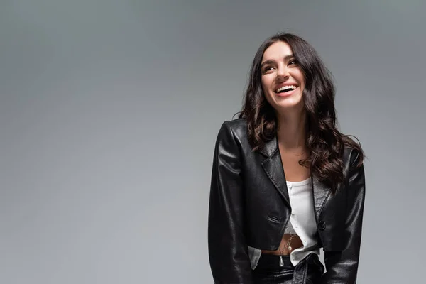 Joyful young woman in stylish black leather jacket and skirt isolated on grey — Stock Photo