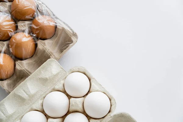 Top view of different eggs in carton boxes with cellophane on white background — Stock Photo
