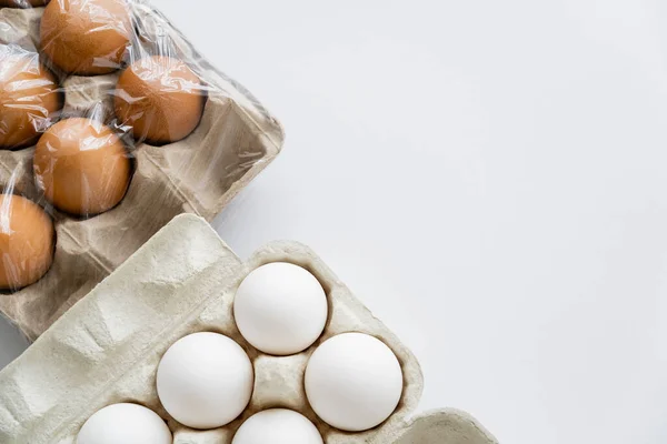 Vista superior de diferentes huevos en cajas de cartón con celofán sobre fondo blanco - foto de stock