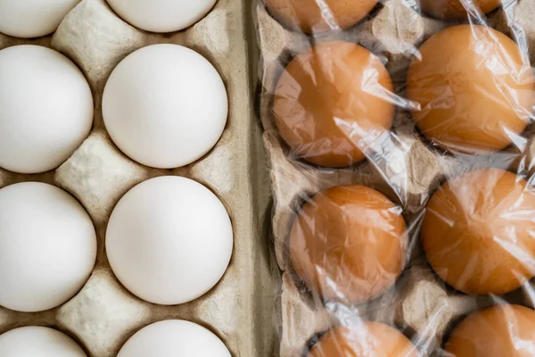 Vista superior de huevos de pollo blancos y marrones en bandejas con celofán - foto de stock