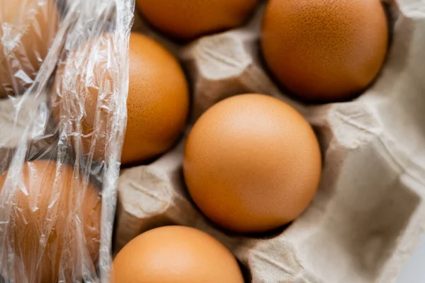 Vue rapprochée des œufs de poule bruns dans un plateau flou avec du cellophane — Photo de stock