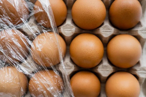 Vista superior de celofán sobre huevos de pollo marrón en recipiente - foto de stock