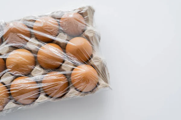 Top view of cellophane on brown eggs in tray on white background with copy space — Stock Photo