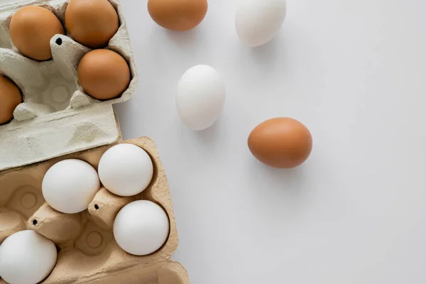 Vue du dessus des œufs en coquilles près des boîtes en carton sur fond blanc — Photo de stock