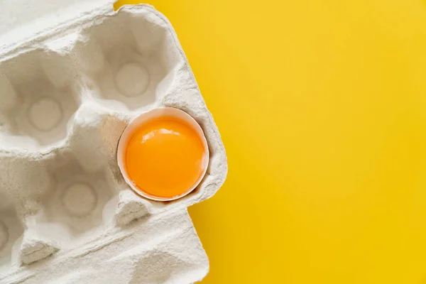 Top view of fresh egg yolk in shell in carton box on yellow background — Stock Photo
